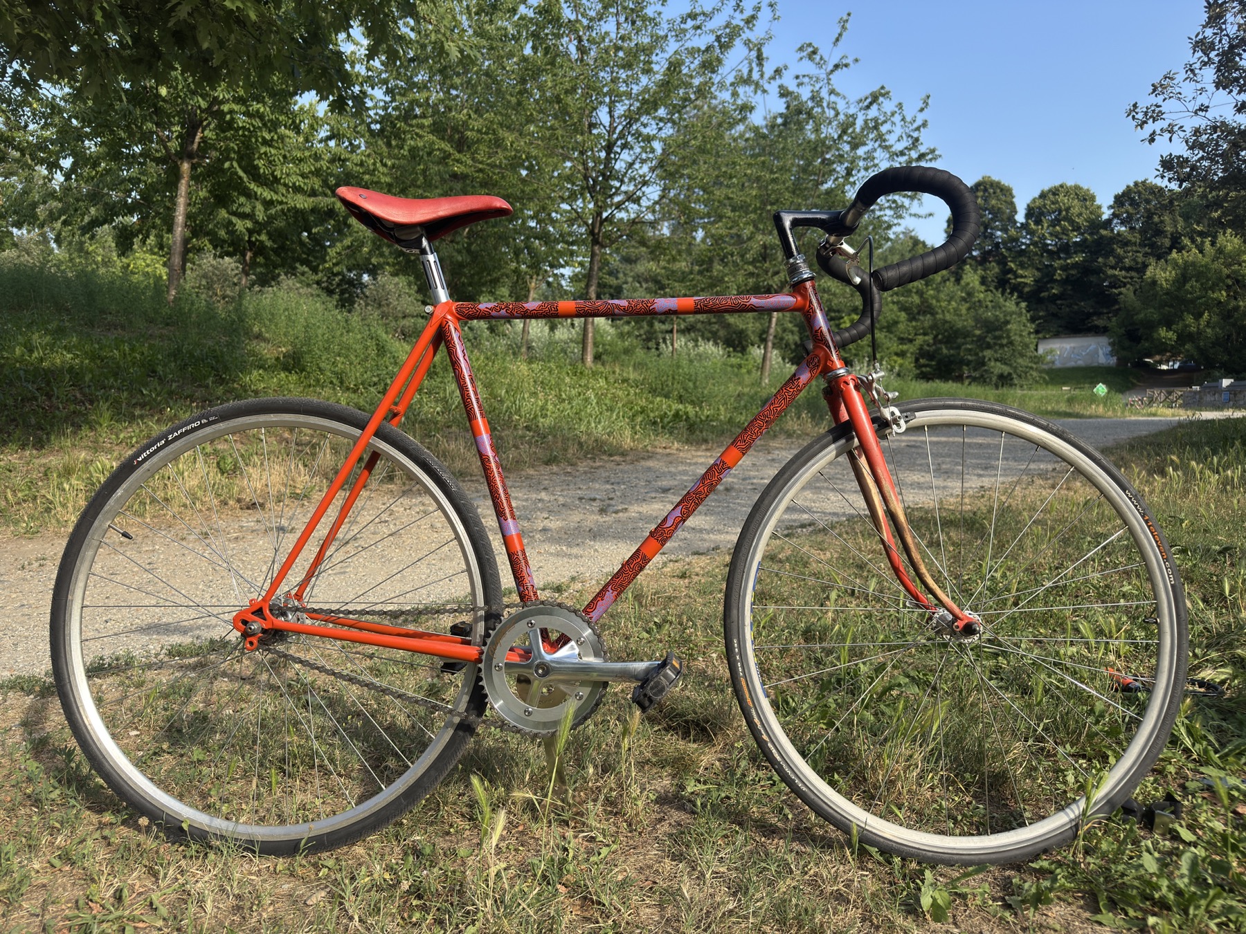 Orange road bicycle painted with intricate black and blue linework in a park